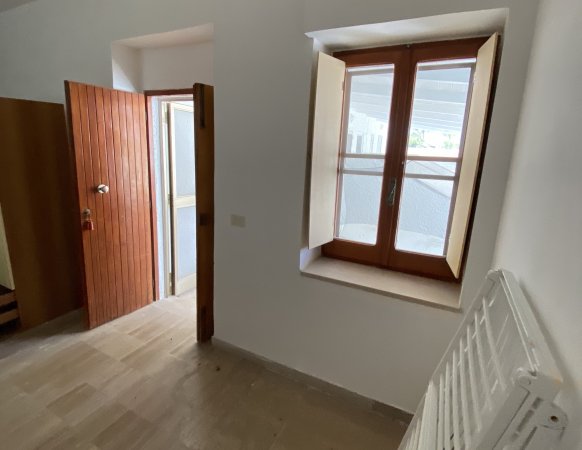 Stanza vuota con porta di legno aperta e finestra a doppio battente.
