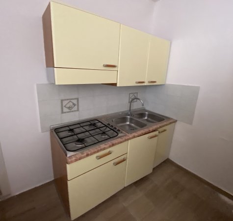 Una piccola cucina con mobili gialli, fornello a gas e lavello doppio.
