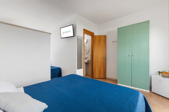 Camera d'hotel con letto matrimoniale, armadio verde, TV e bagno.