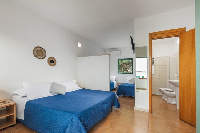 Camera da letto con letto matrimoniale e singolo blu, bagno a vista.