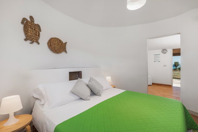 Camera con letto matrimoniale, copriletto verde, lampade e decorazioni a muro.