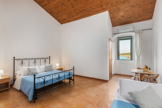 Camera spaziosa con letto matrimoniale in ferro, pavimento in legno e vista sul mare.