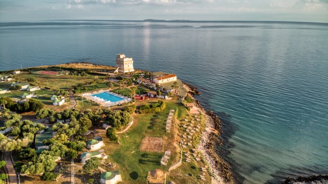Complesso sul mare con piscina, torre, giardini, spiaggia attrezzata e mare calmo.