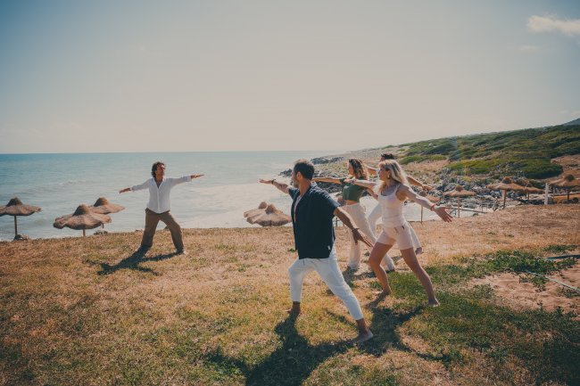 Persone che praticano yoga su un prato vicino al mare, in una giornata soleggiata.