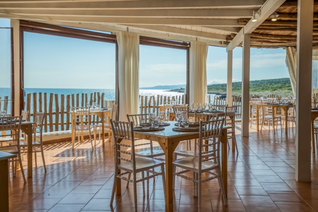 Ristorante con vista sul mare, arredato con sedie trasparenti e tavoli apparecchiati.