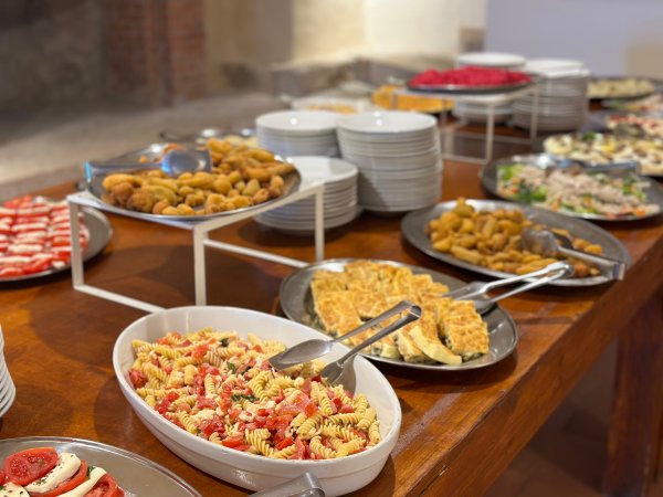Buffet con piatti di pasta, pietanze fritte e vari contorni su un tavolo di legno.