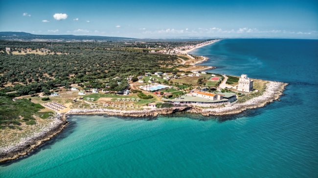 Vista aerea di una costa con edifici, rocce e mare azzurro.