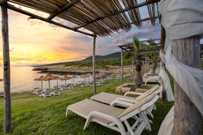 Lettini sotto pergole con vista sul mare al tramonto.
