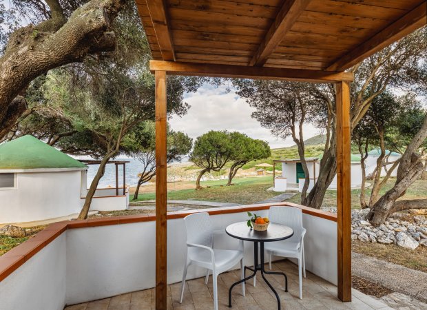 Veranda con tavolo, sedie e vista sul mare tra gli alberi.