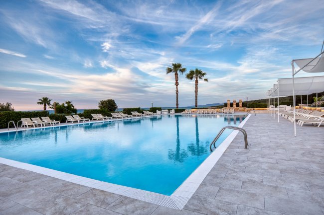 Piscina con lettini e palme sotto un cielo blu.