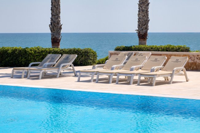 Lettini bianchi vicino a una piscina con vista sul mare e palme sullo sfondo.