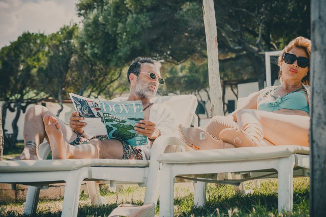Due persone rilassate su lettini all'aperto; una legge una rivista.