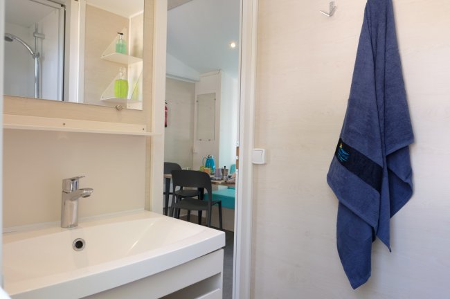 Bagno con lavandino moderno, accappatoio blu appeso e vista su una stanza con tavolo.