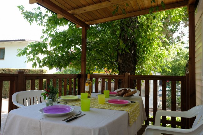 Tavolo apparecchiato su terrazza coperta con vista sul giardino.