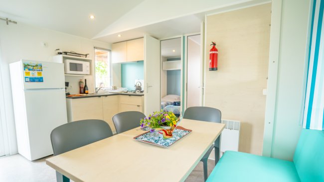 Sala da pranzo con tavolo, sedie, cucina, frigo e fiori al centro.