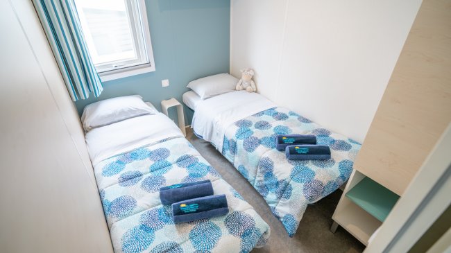 Due letti singoli con lenzuola blu, due asciugamani e un peluche.