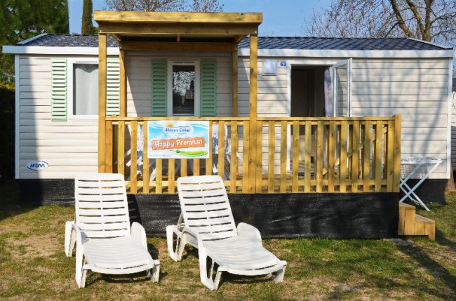 Due lettini prendisole davanti a una casa mobile con veranda in legno chiaro.
