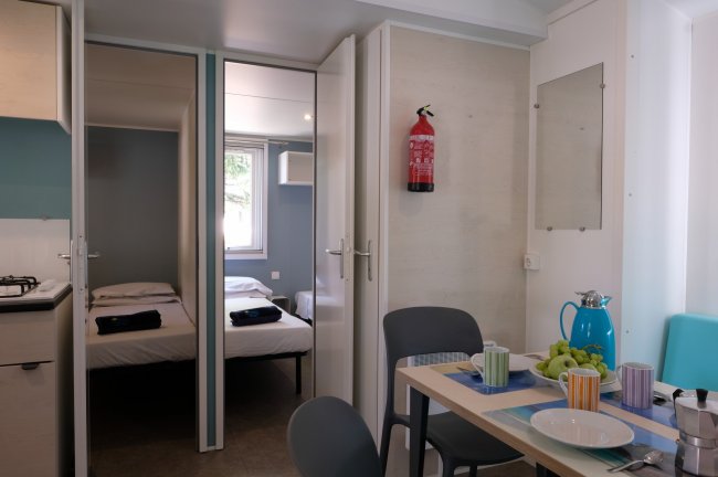 Interno di una casa mobile, tavolo con colazione apparecchiata e vista su una camera doppia.
